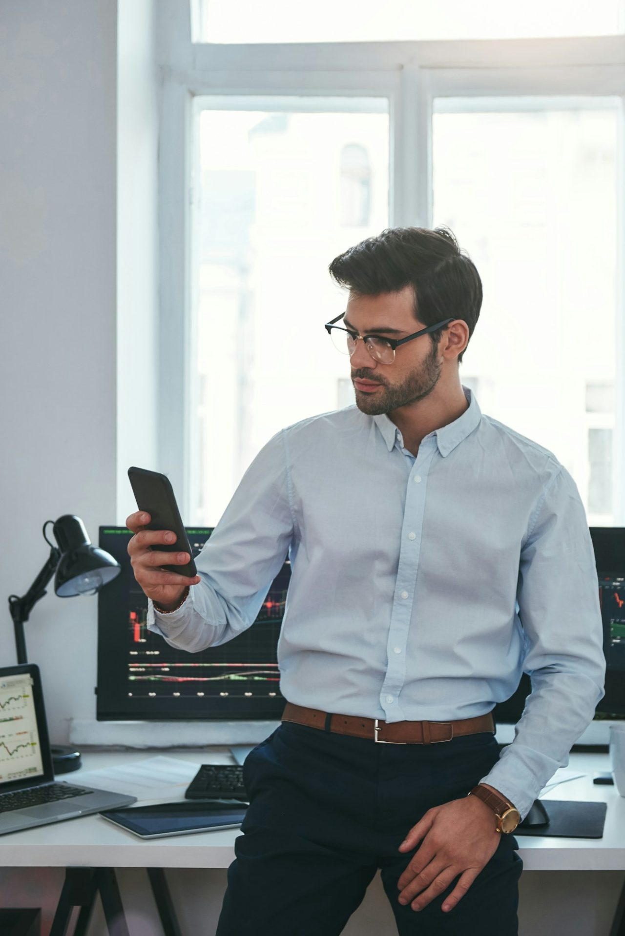 Concentrated young trader in formal wear and eyeglasses is looking at trading graphs